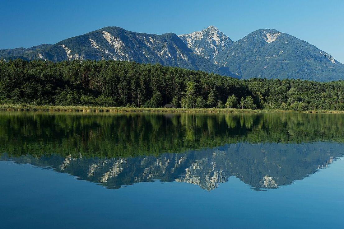 Gebirgslandschaft mit Wald und See, der Berggipfel unter klarem blauen Himmel spiegelt